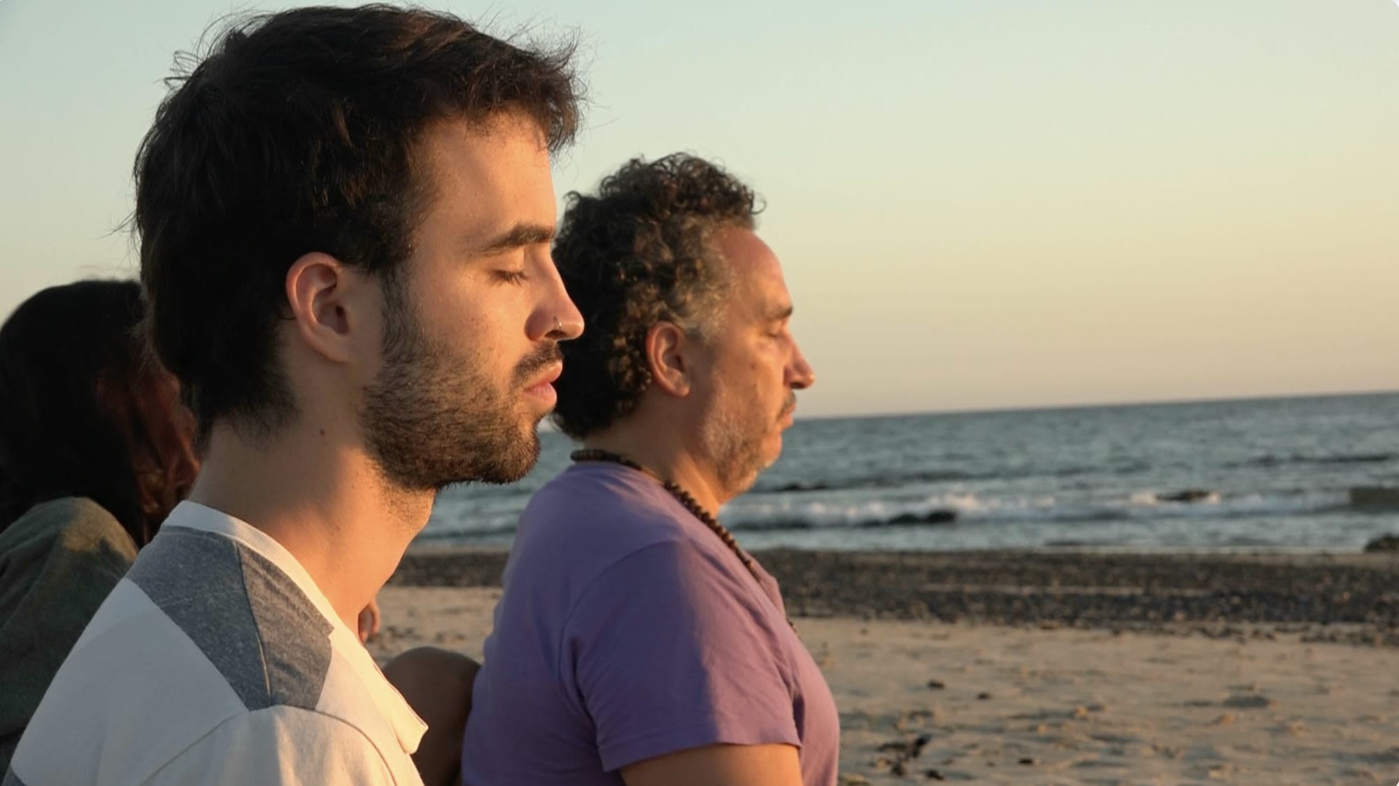 Dos participantes del retiro con los ojos cerrados frente al mar, al atardecer